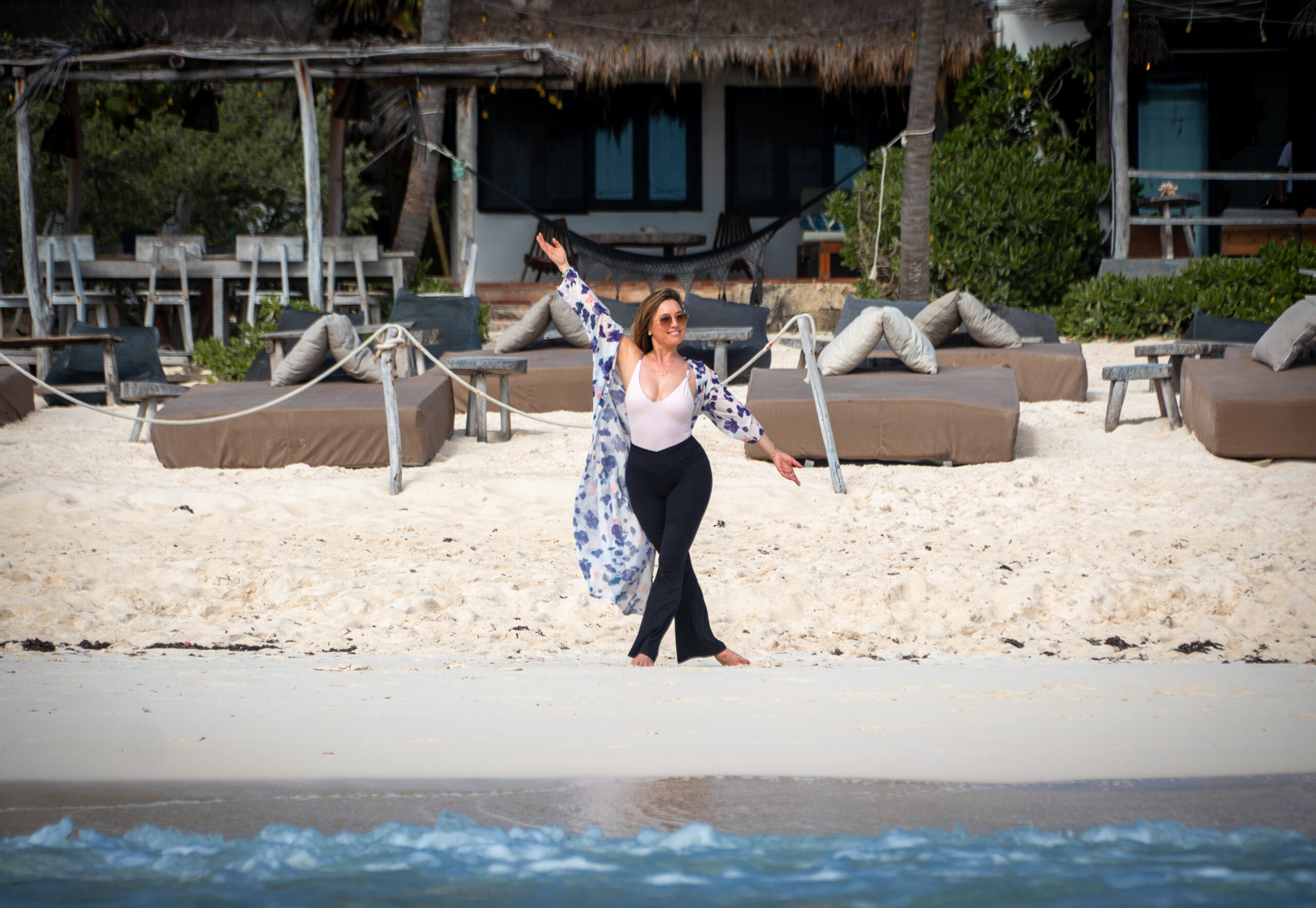 A woman joyfully posing on the beach in Tulum, Mexico, in front of a boutique beachfront resort.