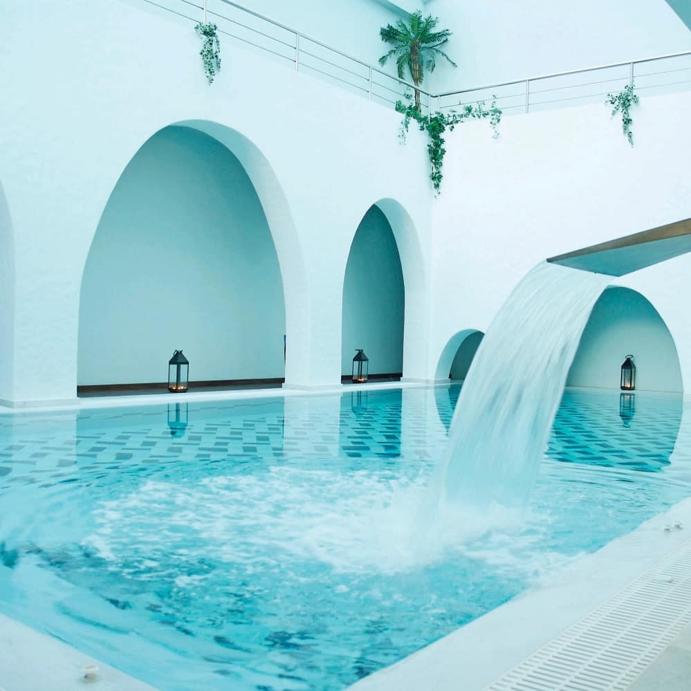 Tranquil indoor pool with waterfall feature and arched white walls at Aegialis Hotel & Spa, Greece.