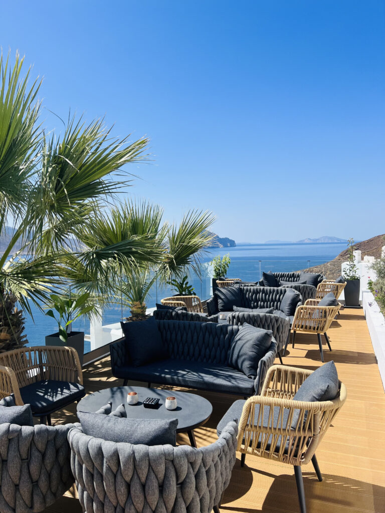 Chic outdoor lounge with cozy seating, palm trees, and panoramic sea views at Goddess Getaway Retreat in Greece.