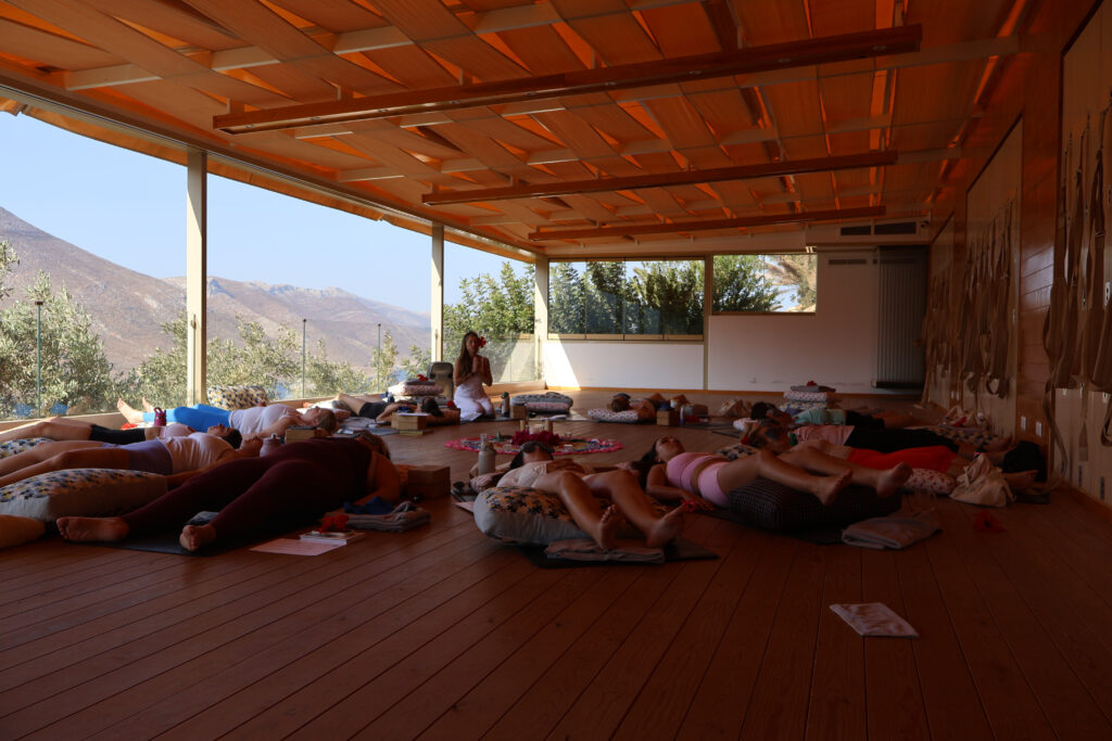 Women in restorative yoga poses with bolsters and eye pillows during Cece Yoga Greece 2025 retreat.