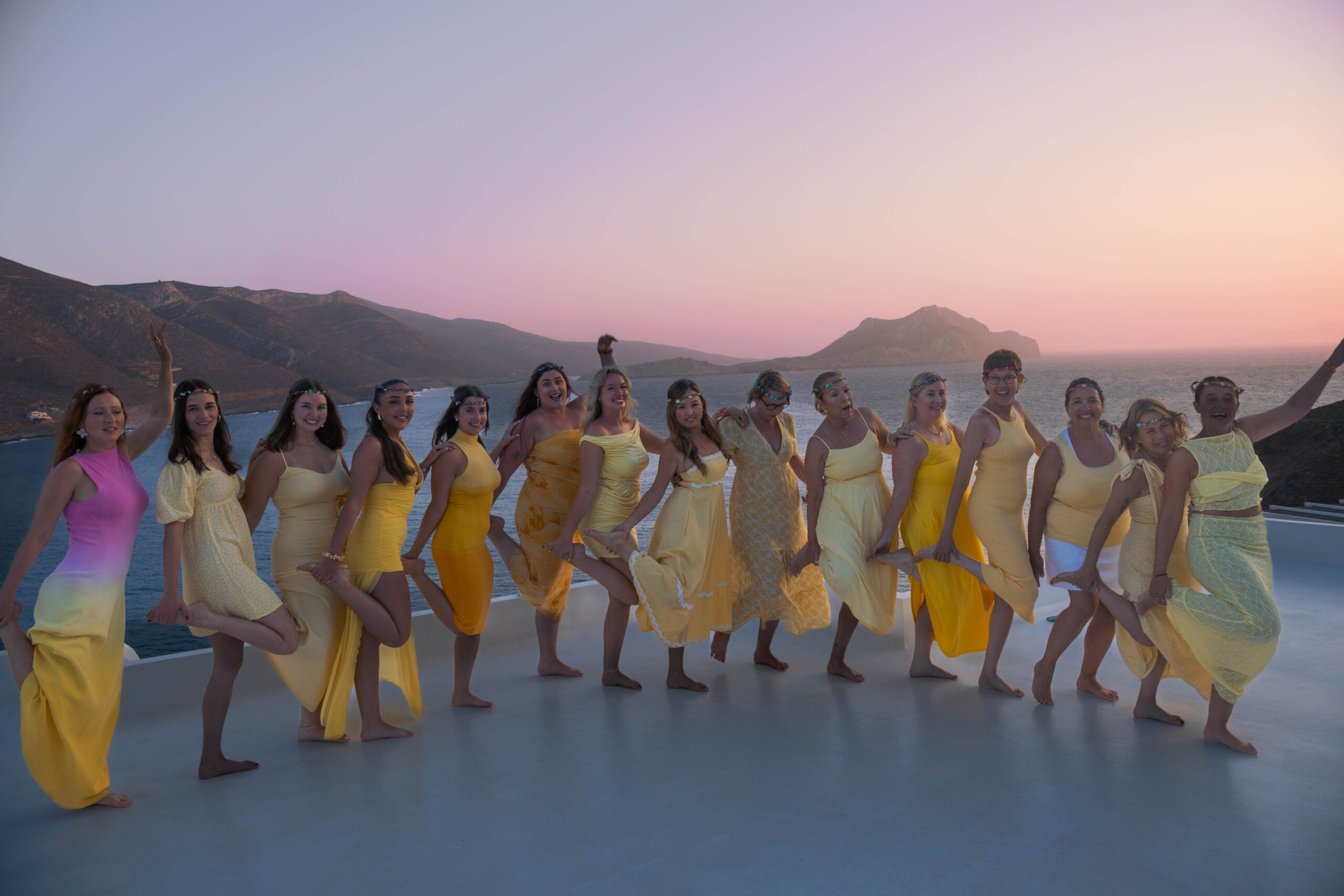 Women in yellow dresses celebrating together by the sea during a Greece yoga retreat